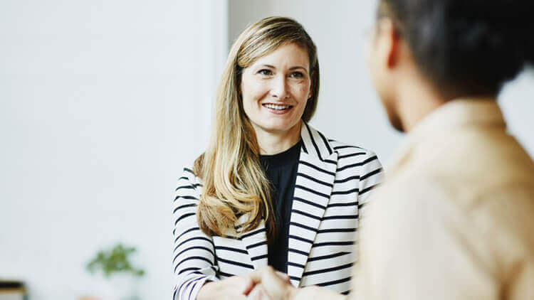 Business woman smiling and shaking someones hand in an office
