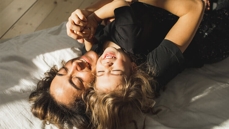 Mother and daughter lying on their backs on a bed laughing together 