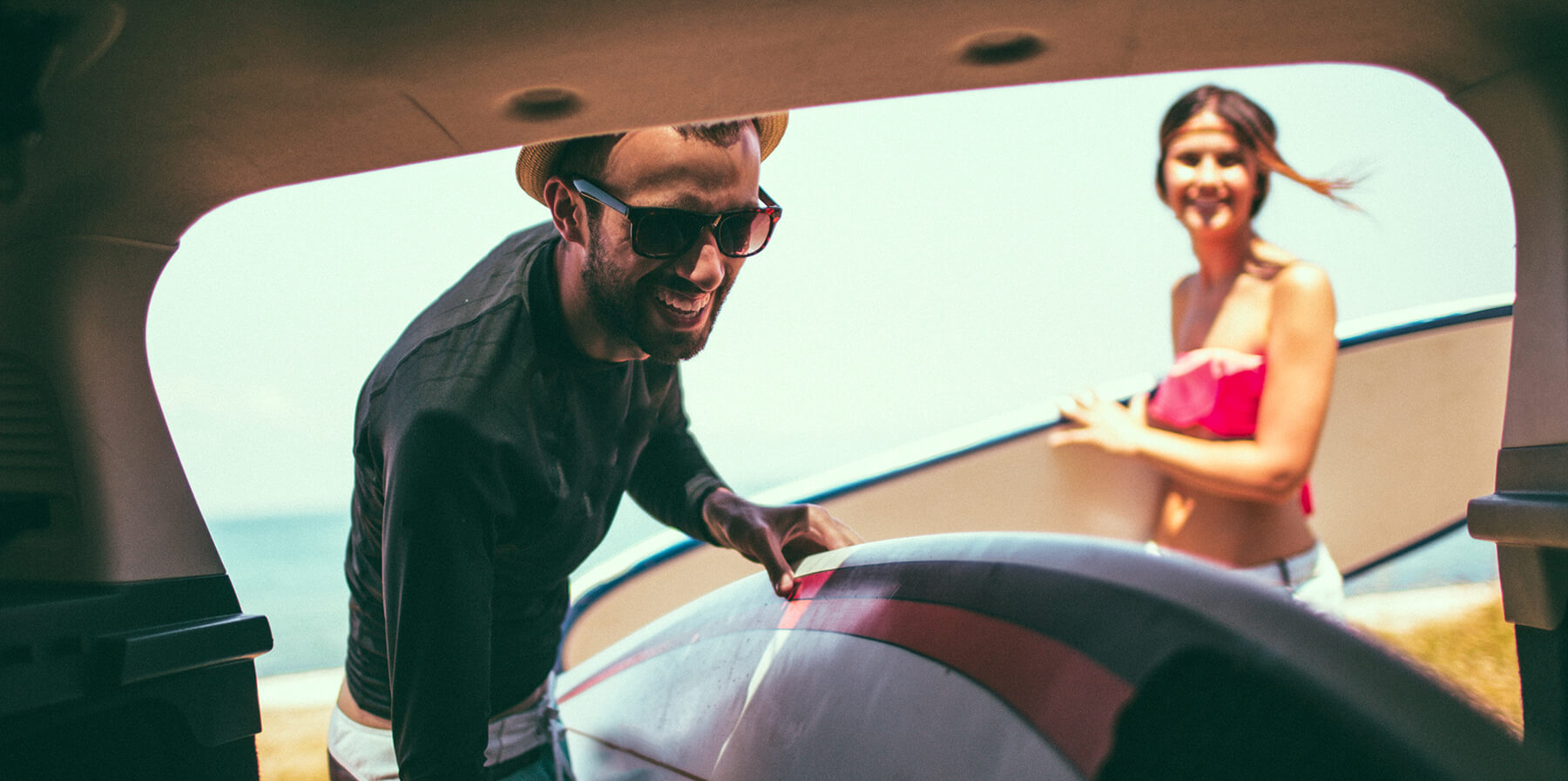 Photo of smiling young people on a road trip, packing their car trunk at the beach