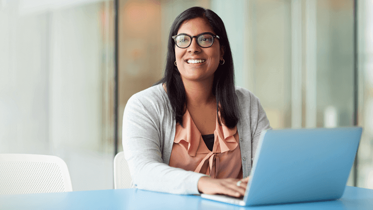 Asian woman in an office looking up smiling on her laptop