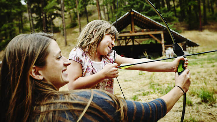 Mother helping daughter take arm using a bow and arrow 