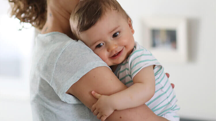 Mother holding her daughter in her arms stood in the kitchen 