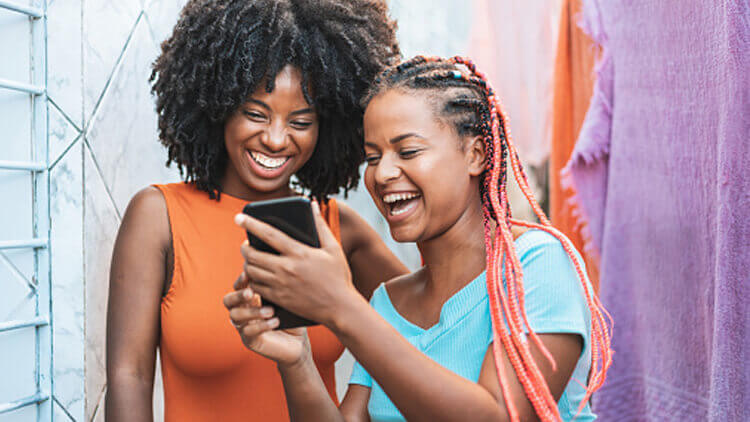 Two Brasilian girls laughing whist looking at a phone