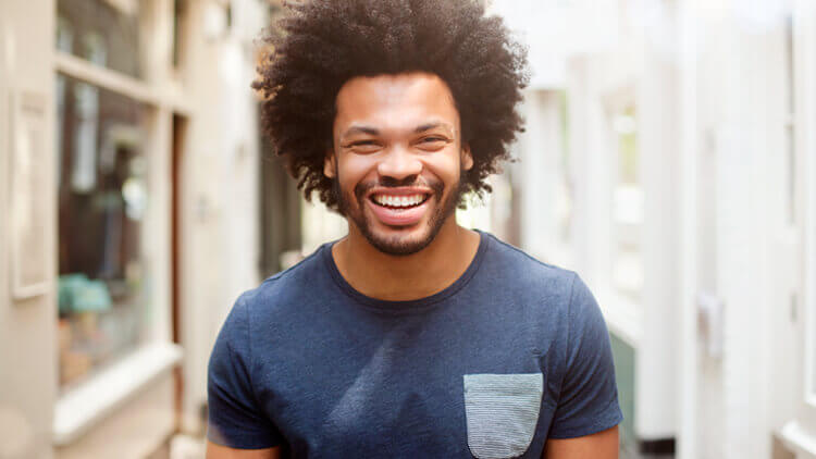 Man with afro hair smiling looking into the camera, walking outside 