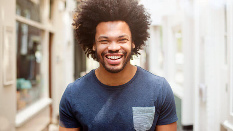Man with afro hair smiling looking into the camera, walking outside 
